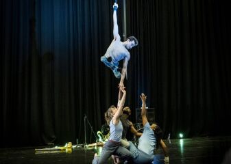 One performer flies on a strap while three other performers reach up to them from the floor.