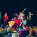 Young people performing in front of an audience, moving and dancing.