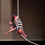 EBYA member Anthony performs an aerial solo with the ropes. He's hanging upside down with limbs reaching out and the rope secured round his waist.