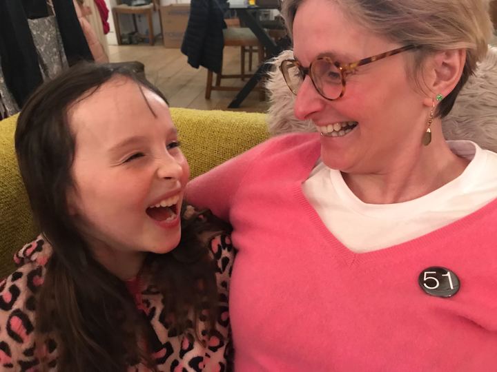 Claire Hodgson sits on the sofa with her young daughter, Scarlett. They are both laughing in an embrace. Claire wears a badge that says '51' - representing 51% of the female population. 