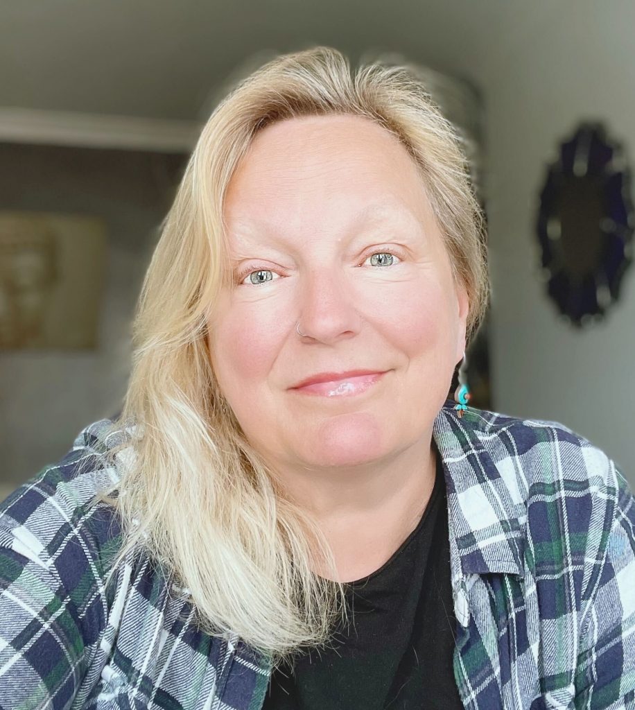 A white woman with blonde shoulder length hair, wearing a checkered shirt.