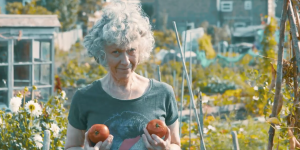 Mid Life: The Skin We're In Karen Spicer, a petite woman with curly grey hair, holds two ripe tomatoes up in front of her chest, as she stands in her allotment.