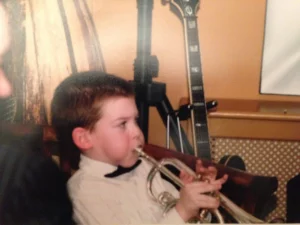 Harry Bassett as young musician holding a trumpet, wearing a bow tie and it's a very old vintage style image.